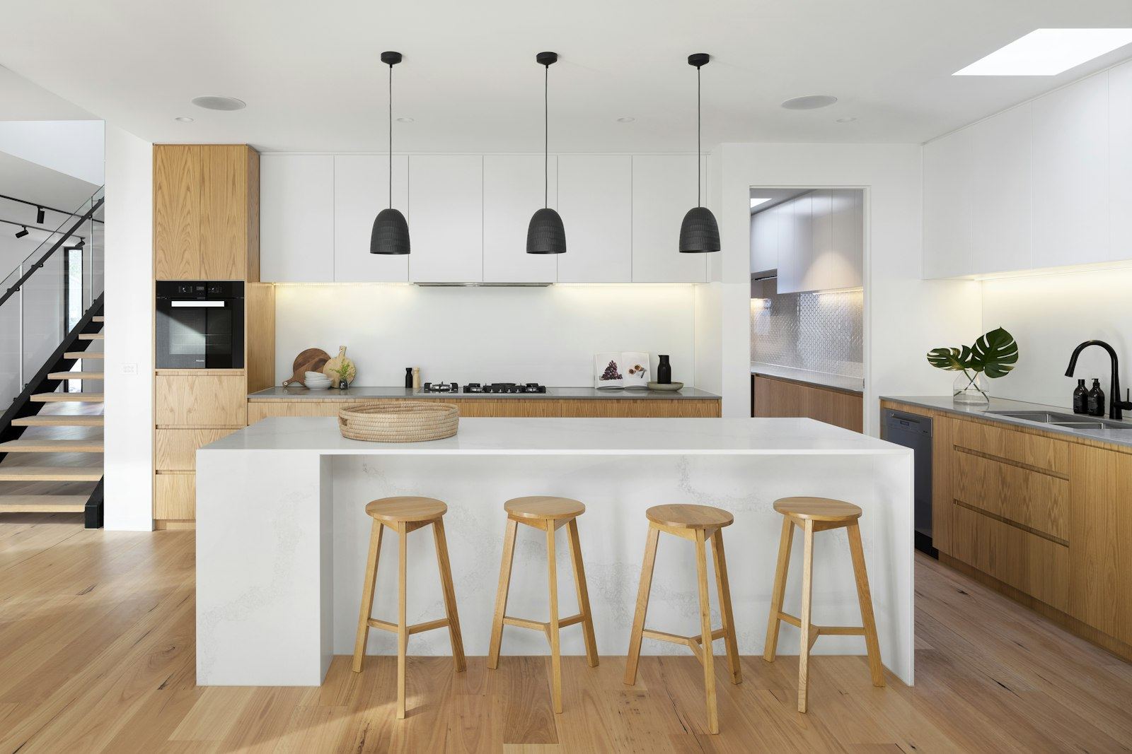 Helle, moderne Küche mit Kochinsel, Holzschränken und schwarzen Pendelleuchten